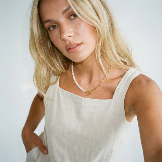 Woman wearing a white sleeveless top and pearl necklace against a plain background