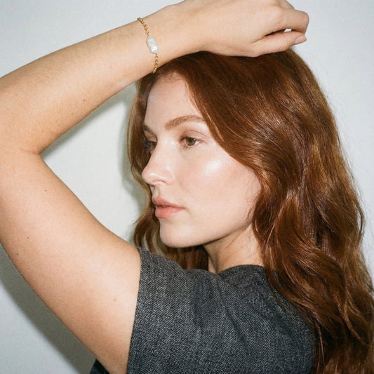 Woman with long brown hair touching her head against a plain background