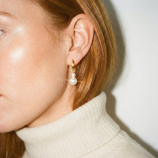 Close-up of a person wearing a pearl earring with a neutral background