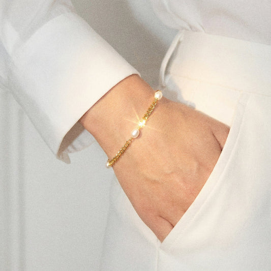 Gold bracelet with pearls on a wrist against a white background