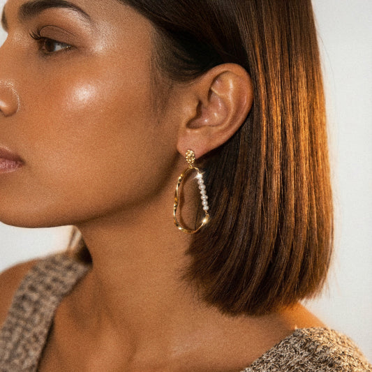 Close-up of a woman wearing a gold hoop earring with a pearl-like center.