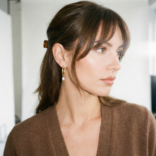 Woman with styled hair and earrings, wearing a brown top.