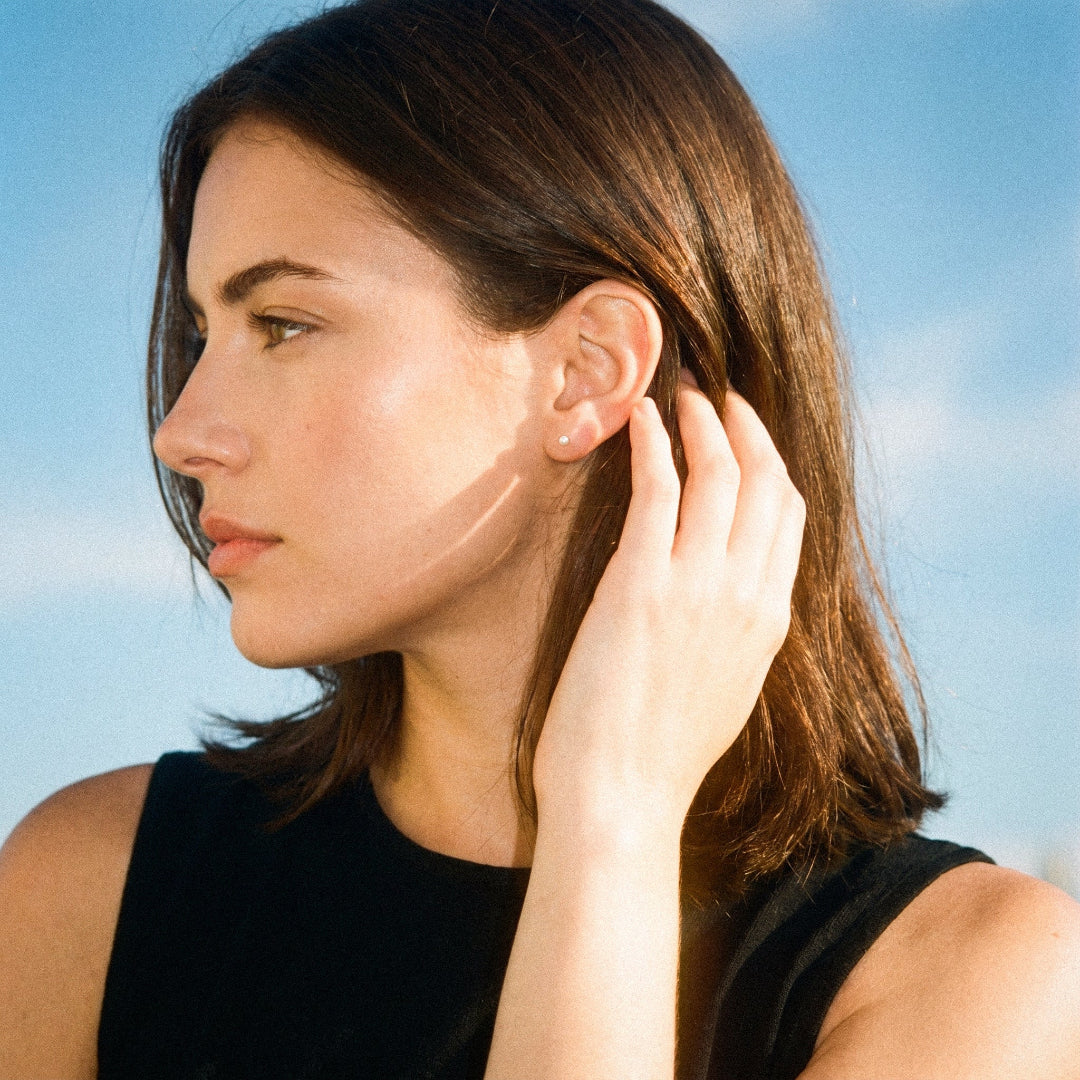 Woman adjusting an earring against a clear blue sky