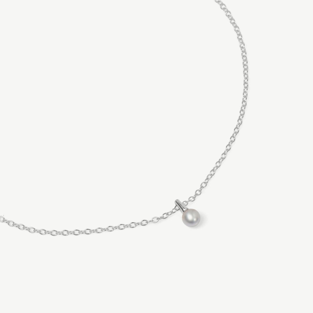 Silver necklace with a single pearl pendant on a light gray background