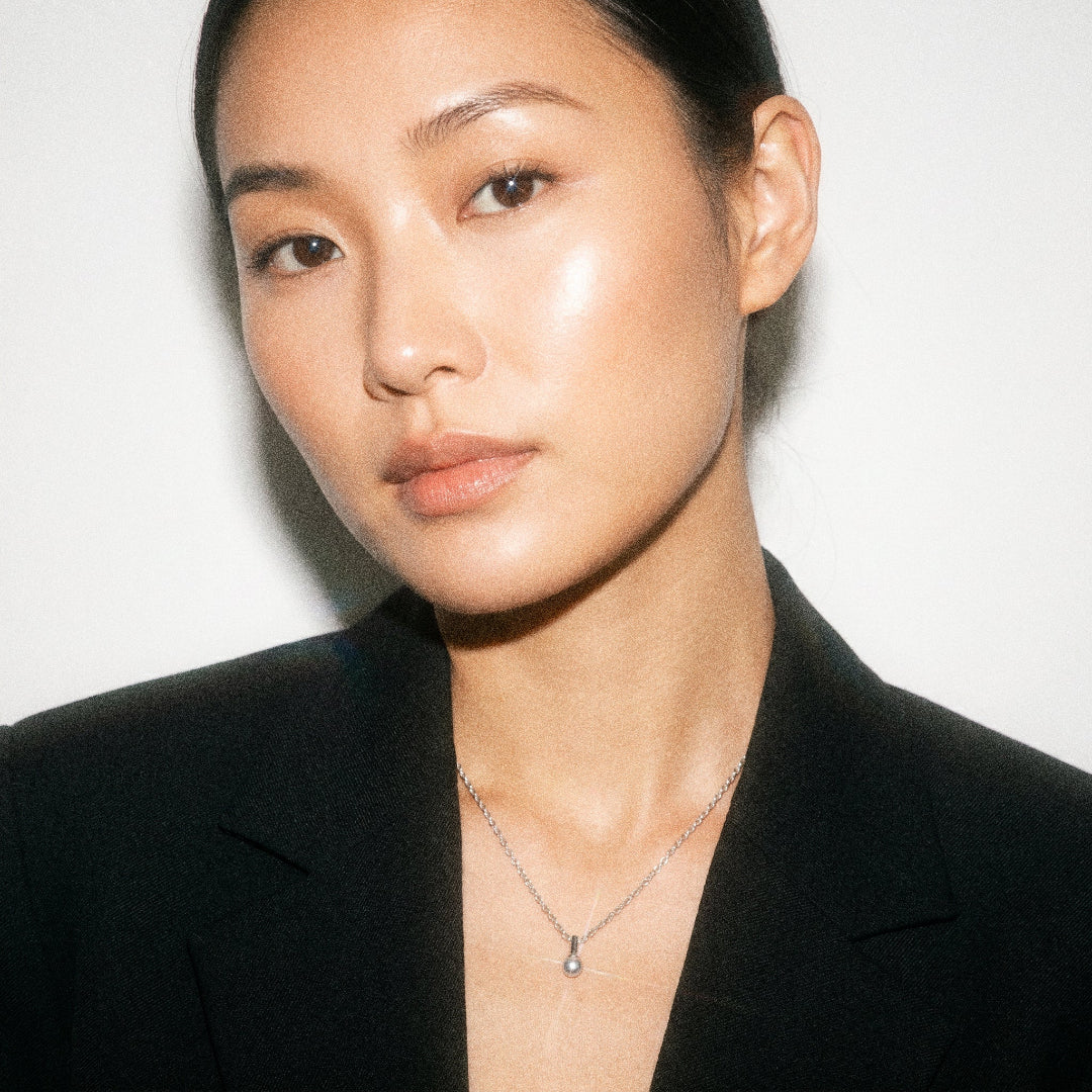 Person wearing a black blazer and silver necklace against a white background