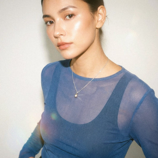 Woman wearing a blue sheer top with a plain background