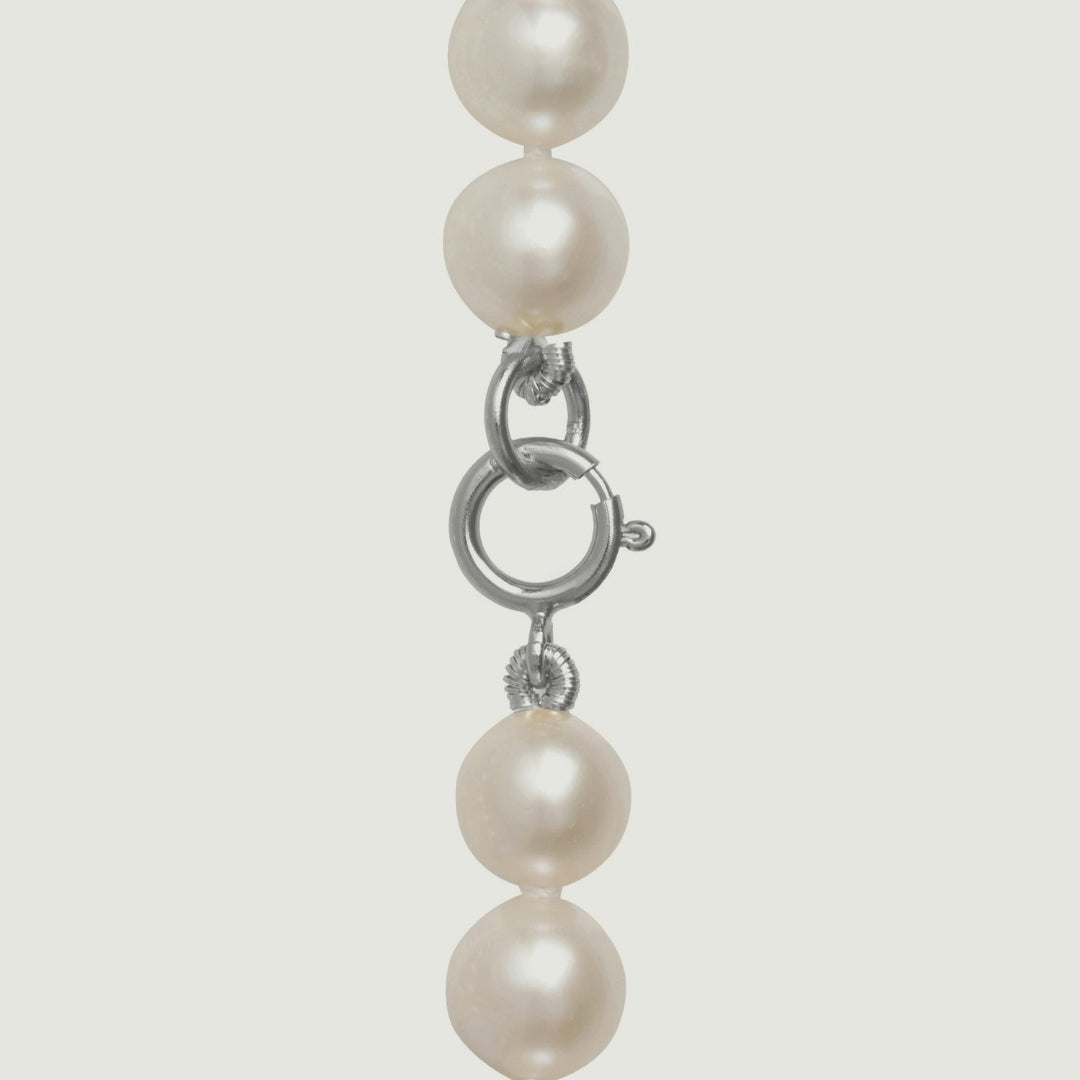 Pearl necklace with a silver clasp on a light gray background