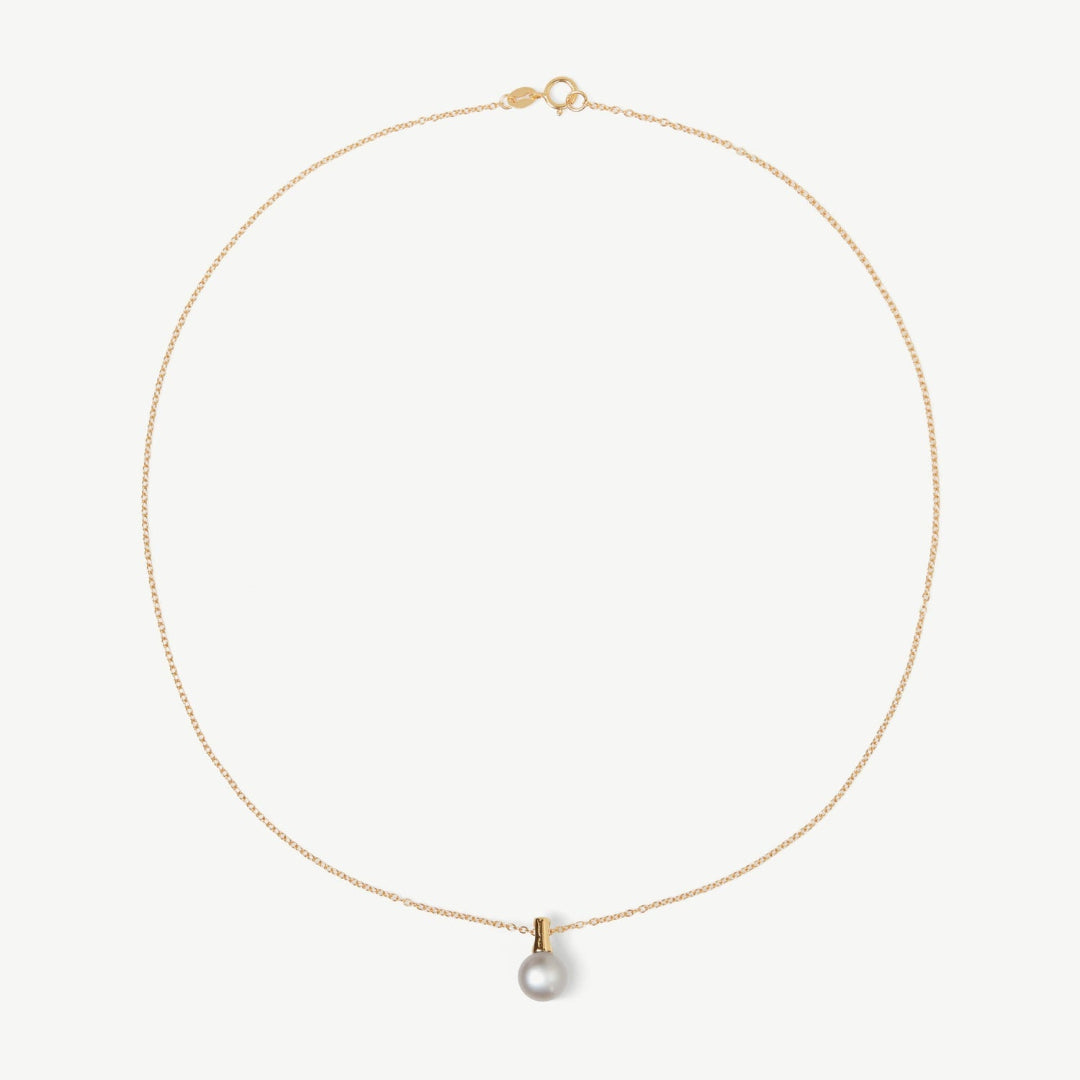 Gold necklace with a single pearl pendant on a light beige background
