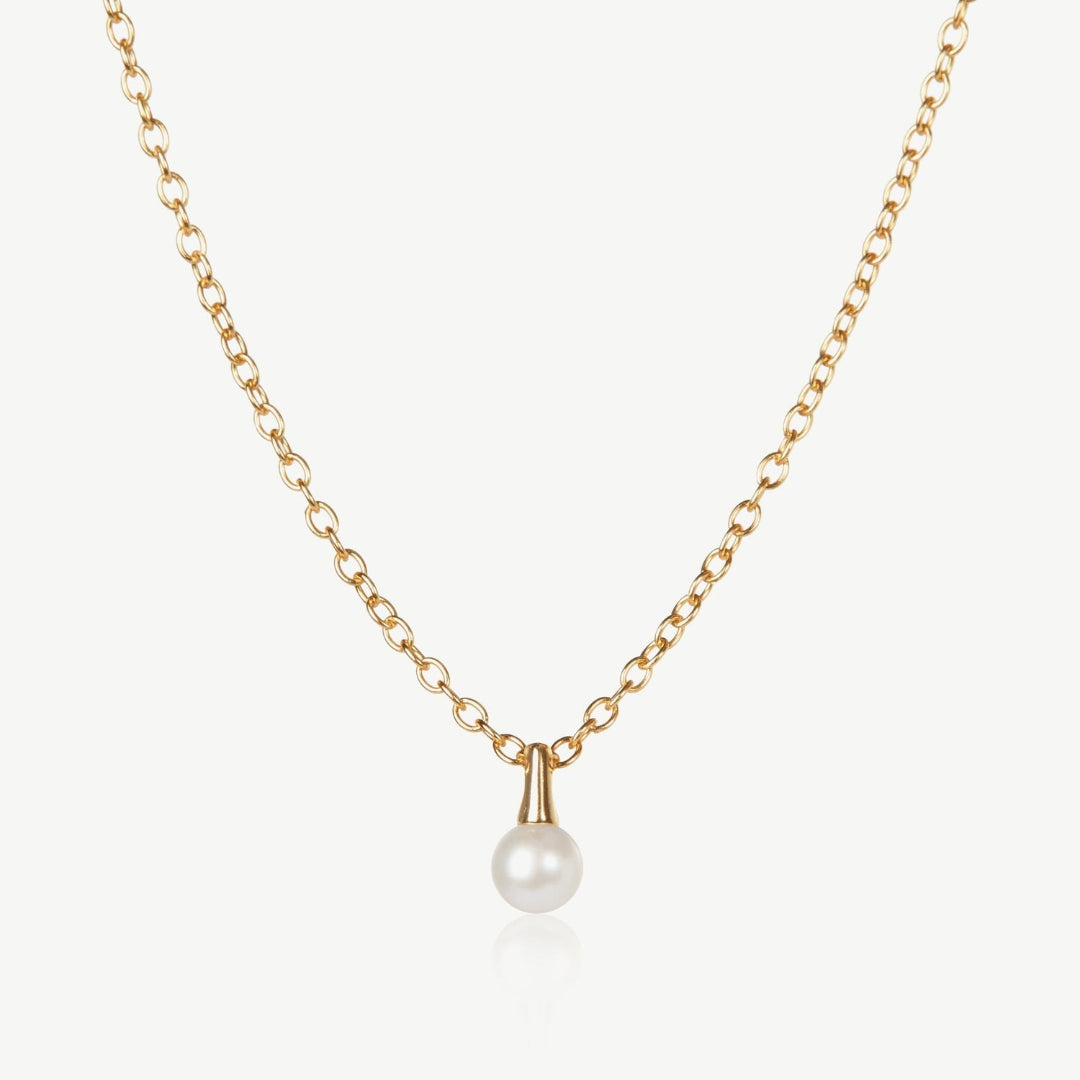 Gold necklace with a single pearl pendant on a light beige background