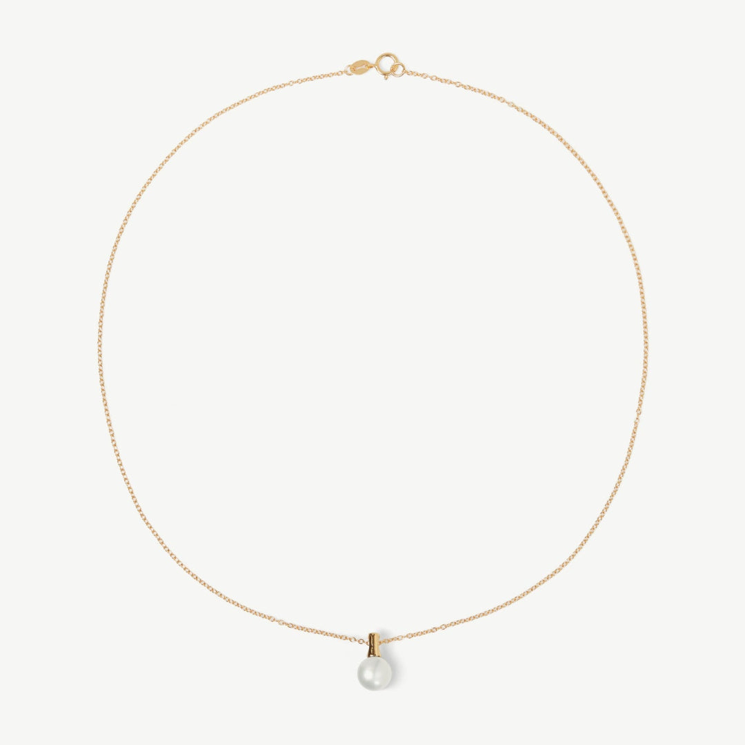 Gold necklace with a single pearl pendant on a light beige background