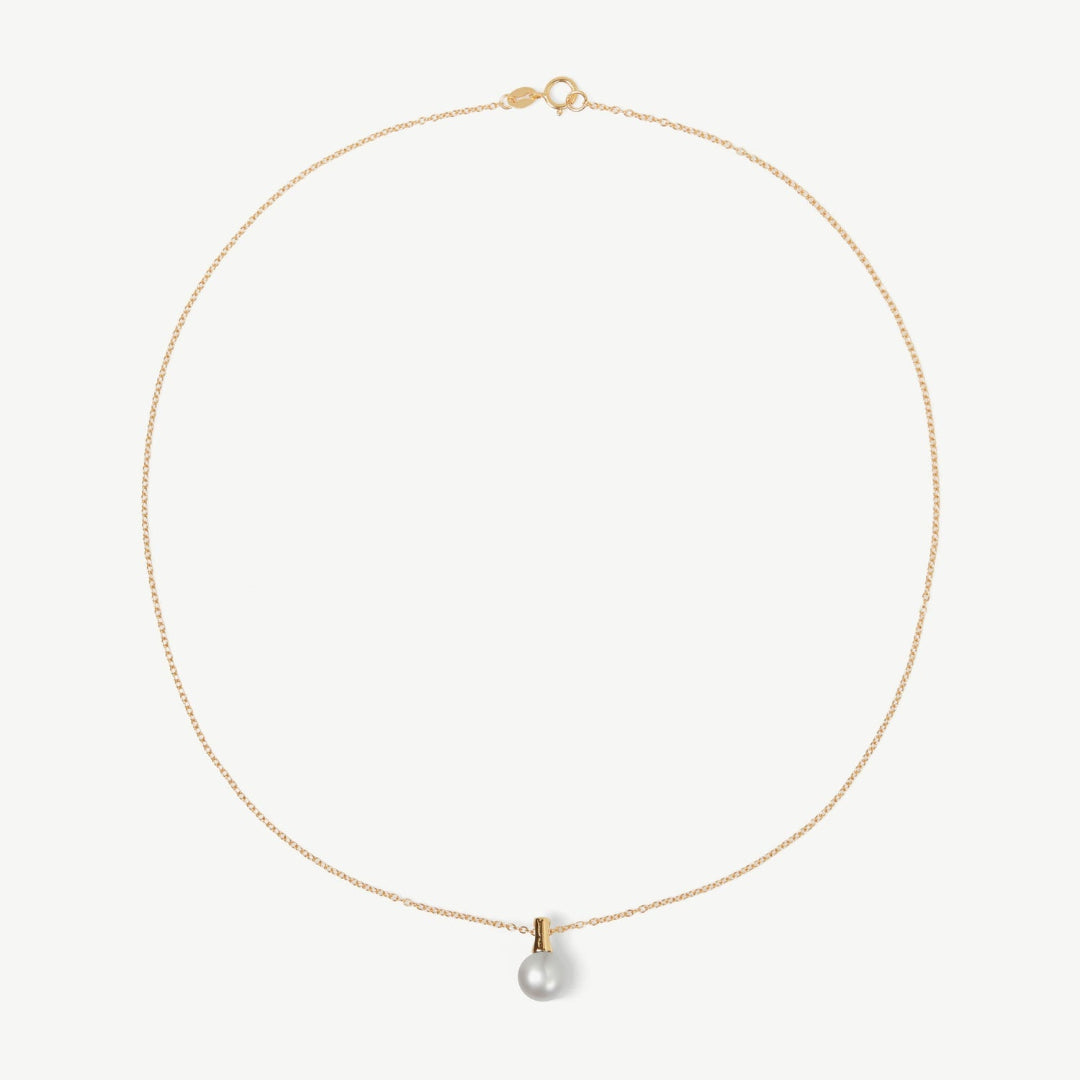 Gold necklace with a single pearl pendant on a light beige background
