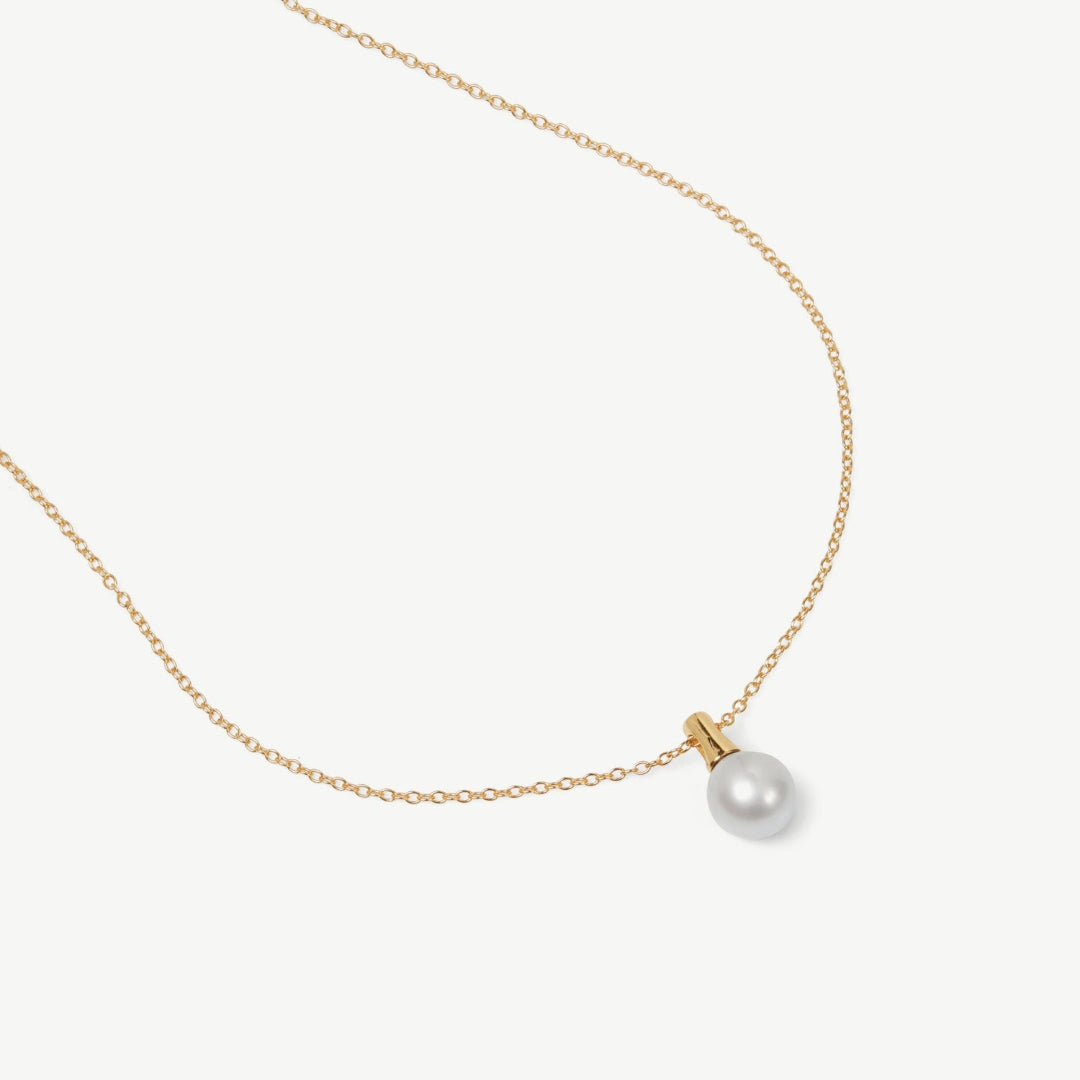 Gold necklace with a single pearl pendant on a white background