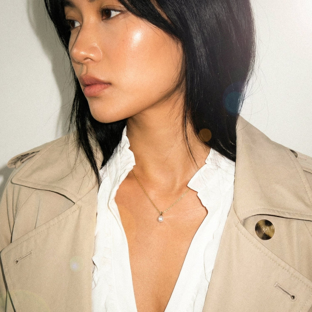 Woman wearing a beige trench coat over a white shirt with a plain background