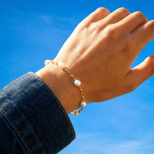 Hand wearing a pearl bracelet against a blue sky