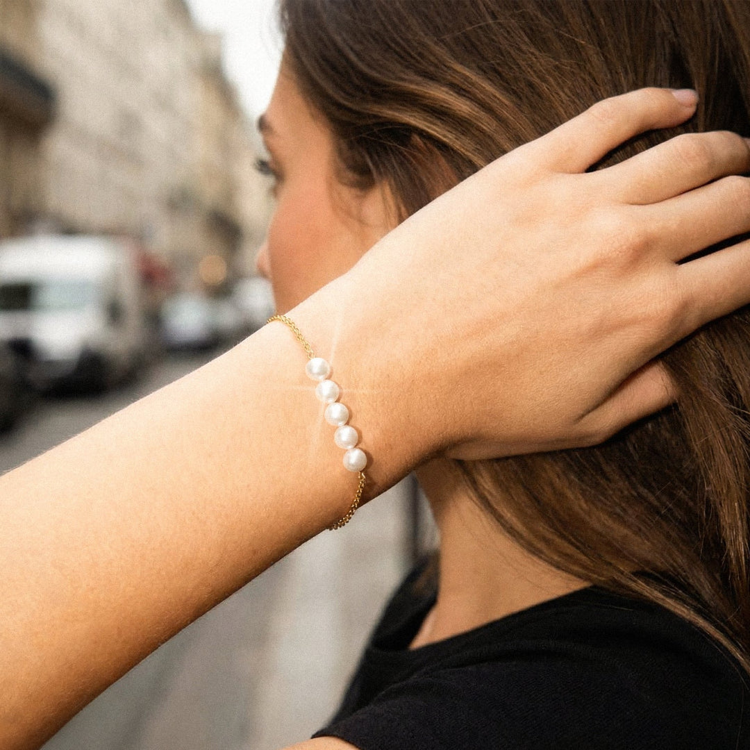 Person wearing a pearl bracelet with a blurred street scene in the background
