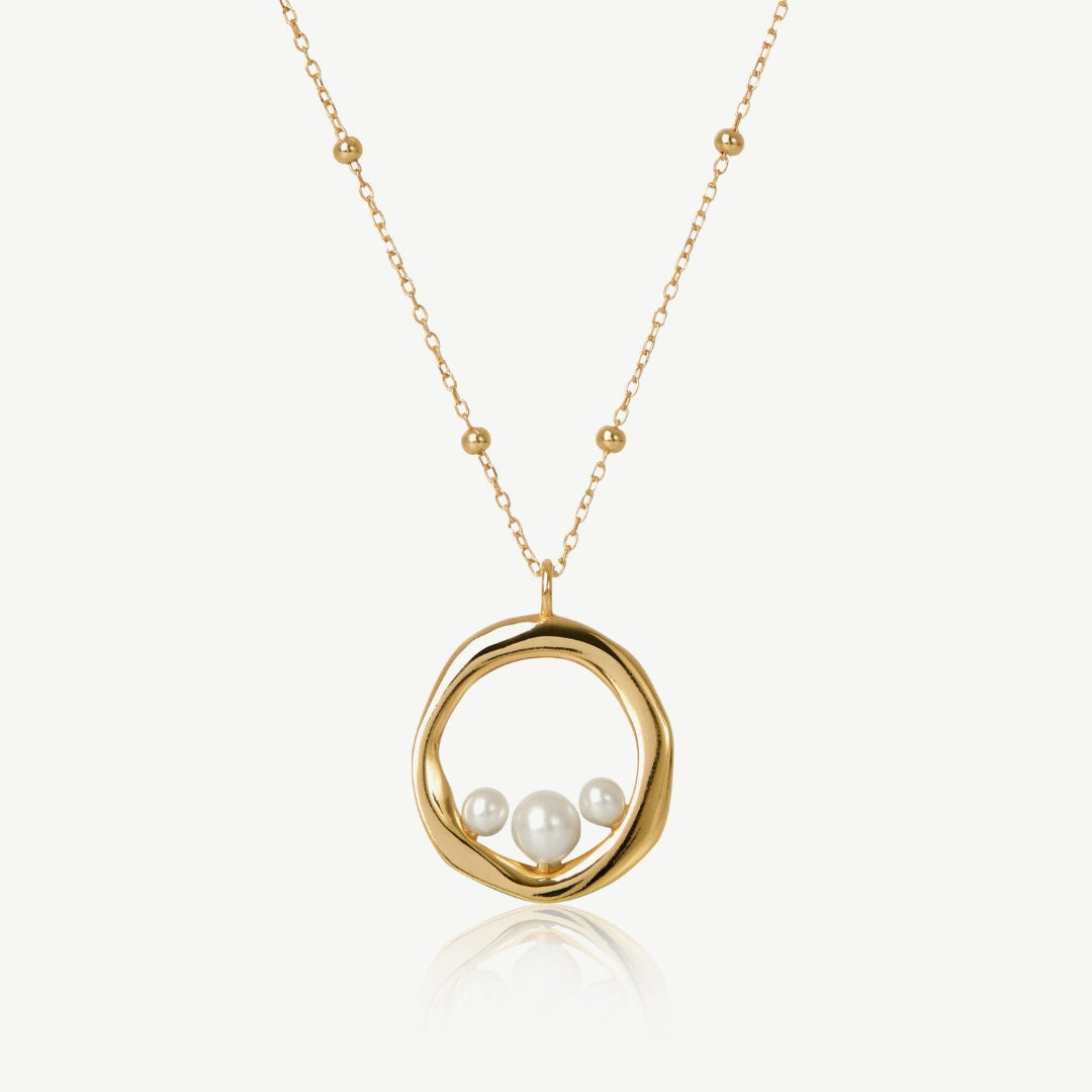 Gold necklace with a circular pendant featuring three pearls on a white background