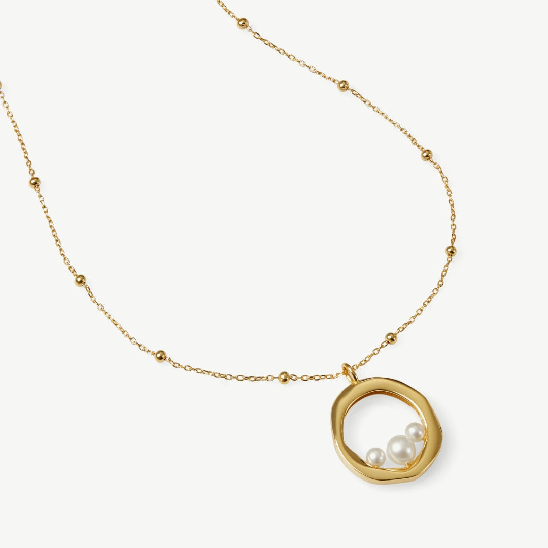 Gold necklace with a circular pendant featuring two pearls on a white background