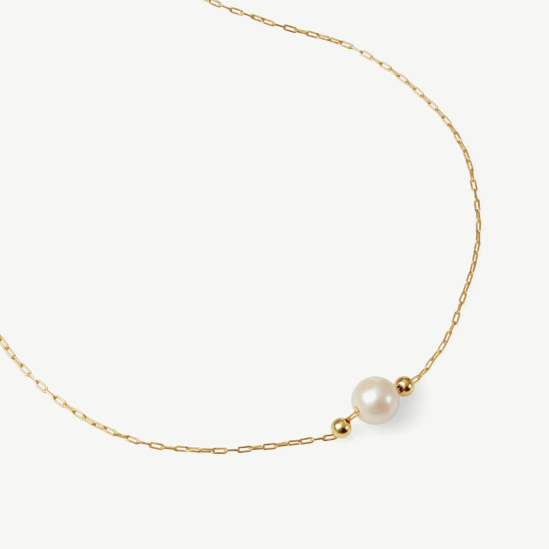 Gold necklace with a single pearl on a white background