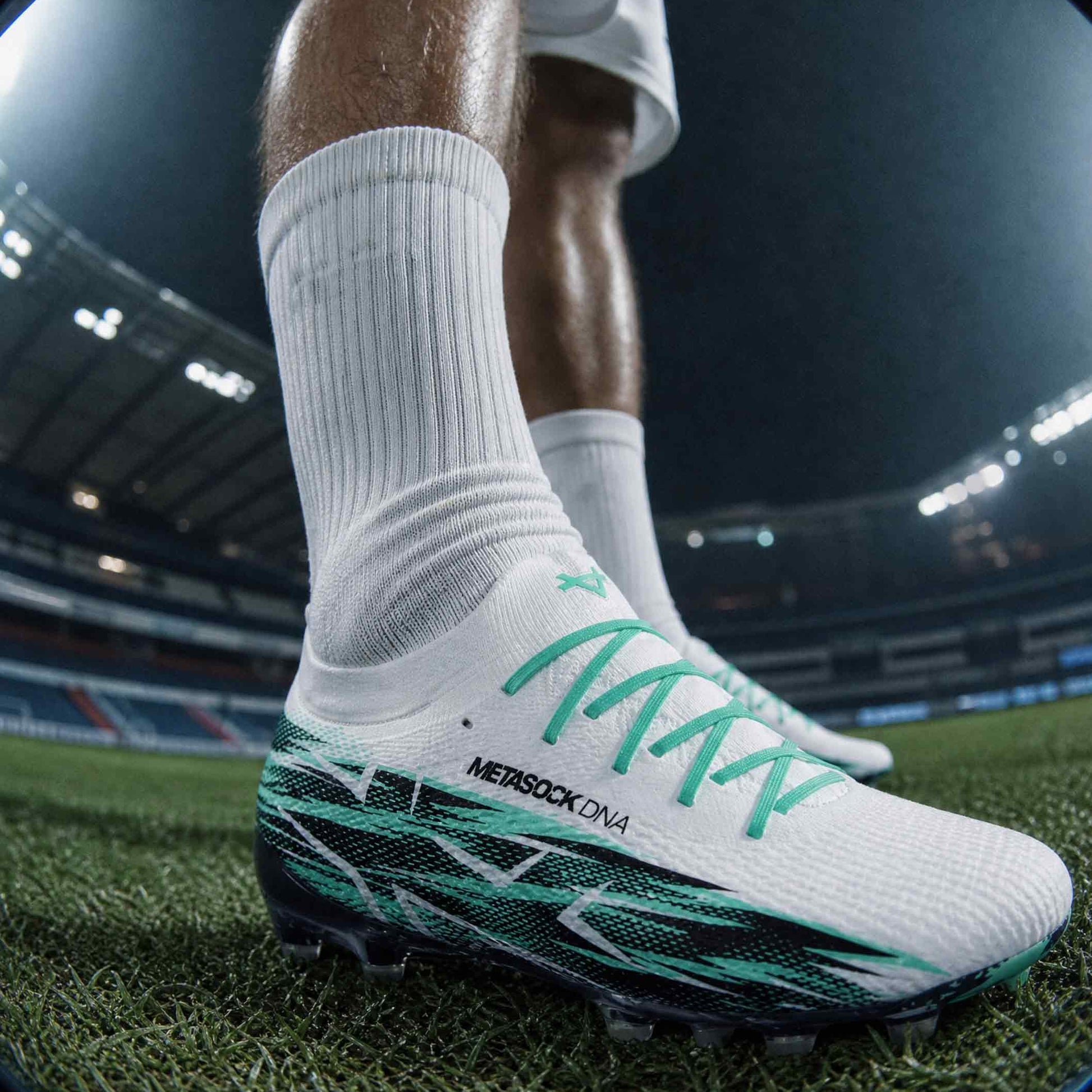Close-up of a soccer player's foot wearing a white and green cleated shoe on a soccer field.