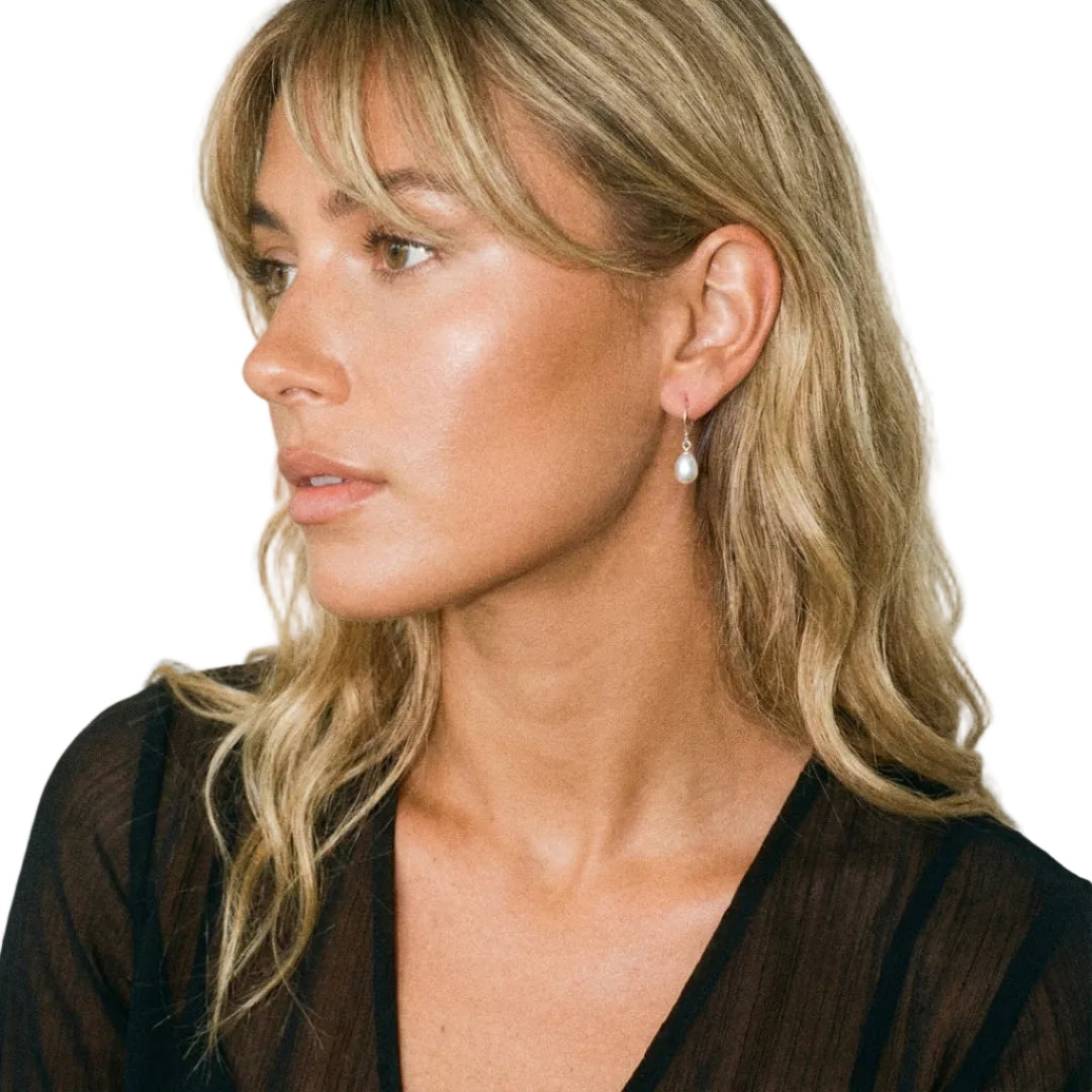 Woman wearing a pearl earring against a plain background