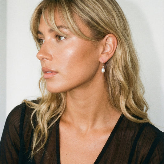 Woman wearing a pearl earring against a plain background