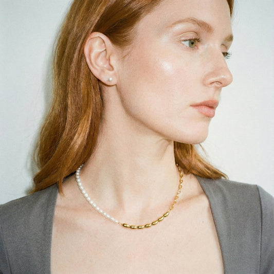 Woman wearing a pearl necklace and gold chain, with a plain background