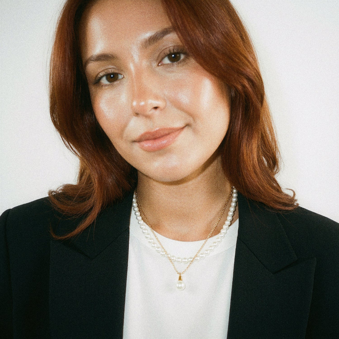 Woman wearing a black blazer and pearl necklace against a white background