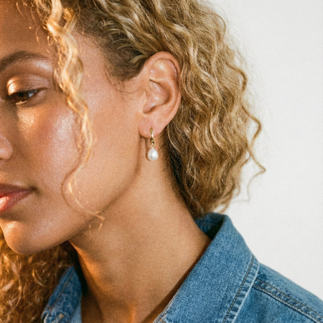 Close-up of a person wearing pearl earrings with a blurred background