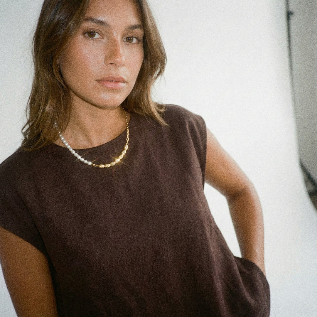 Woman wearing a brown top and gold necklace against a neutral background