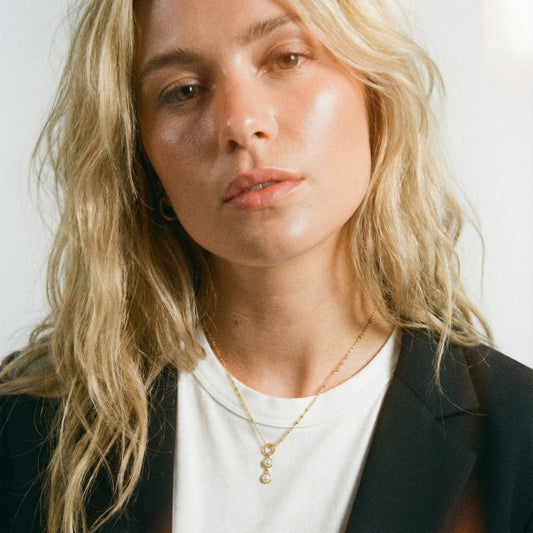 Woman with blonde hair wearing a black blazer and white shirt against a plain background