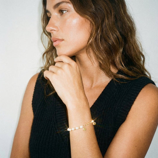 Woman wearing a black sleeveless top and gold bracelet against a plain background