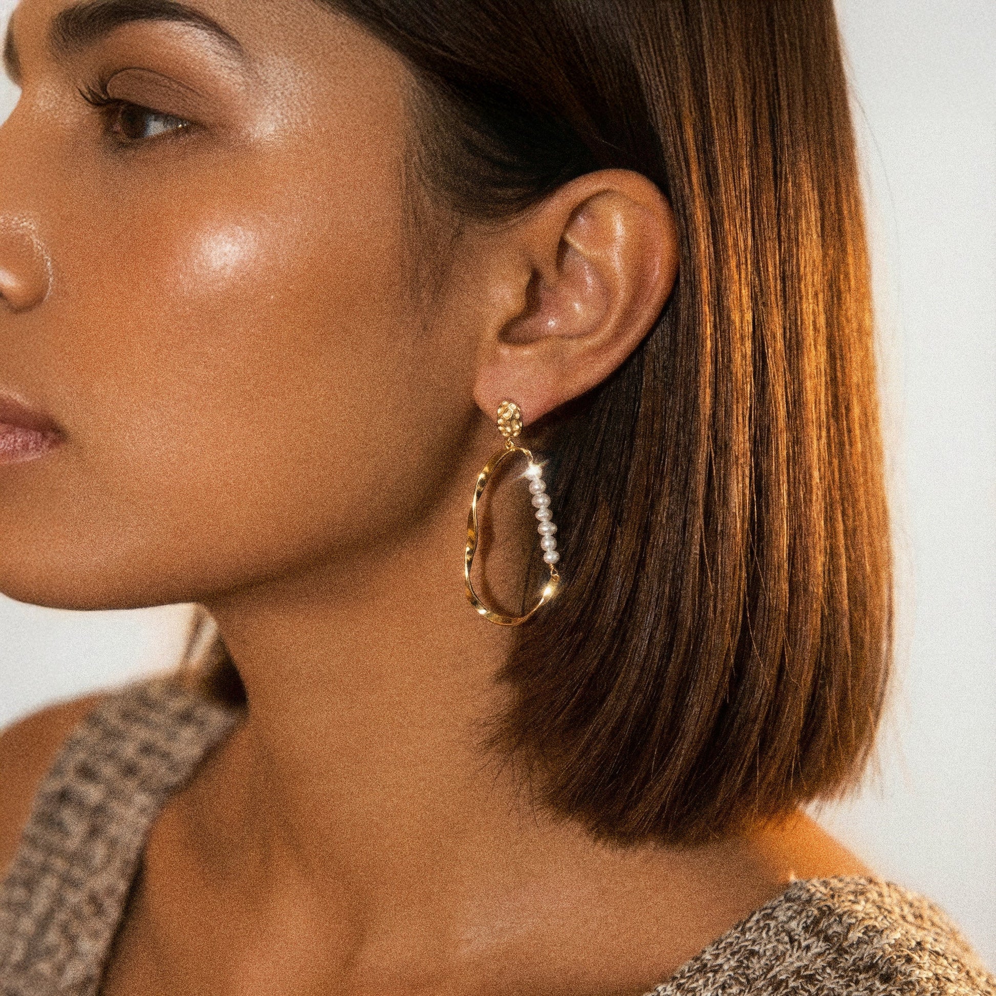 Close-up of a woman wearing a gold hoop earring with a pearl-like center.