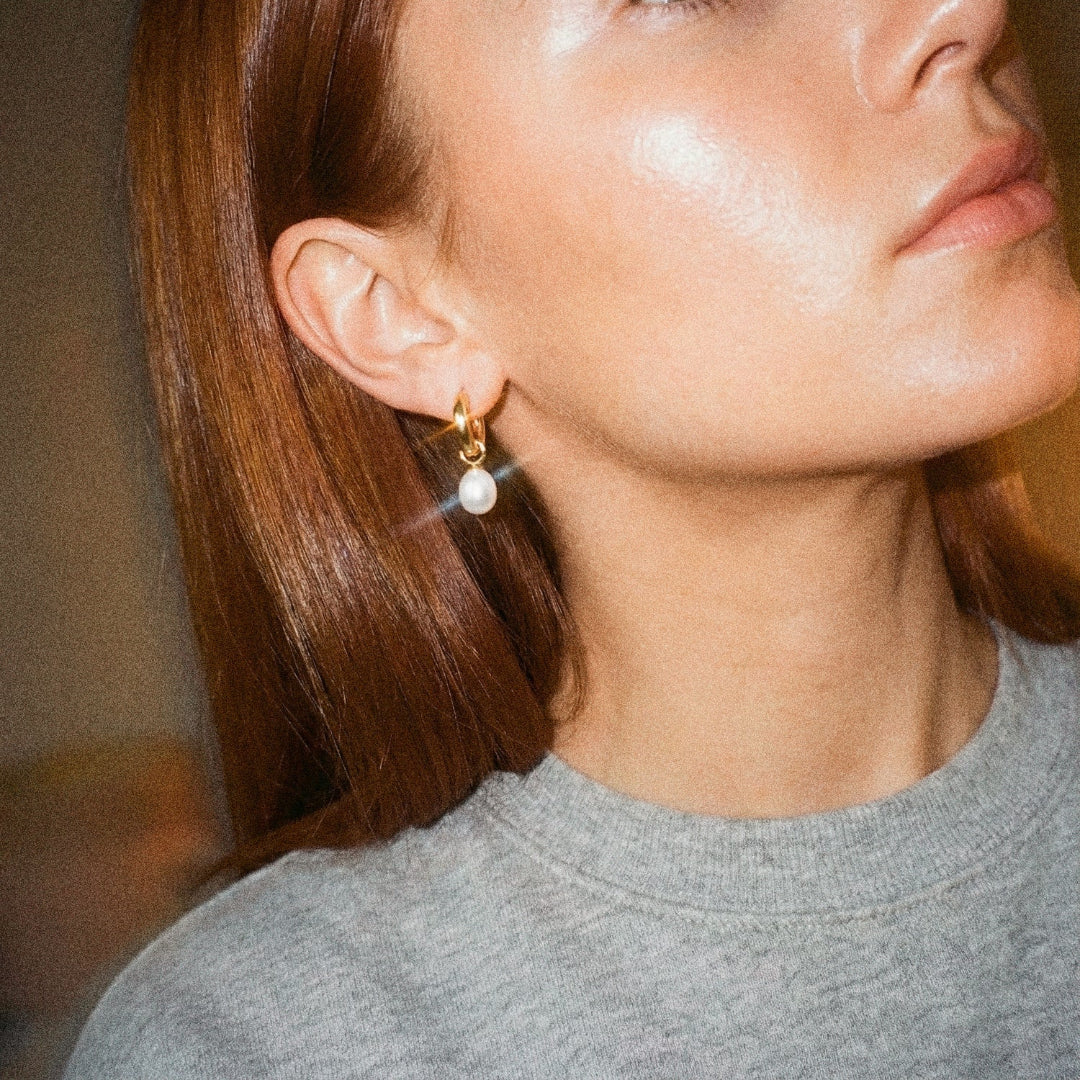 Close-up of a person wearing gold earrings with a blurred background