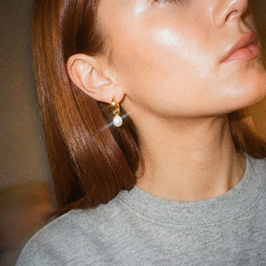 Close-up of a person wearing gold earrings with a blurred background